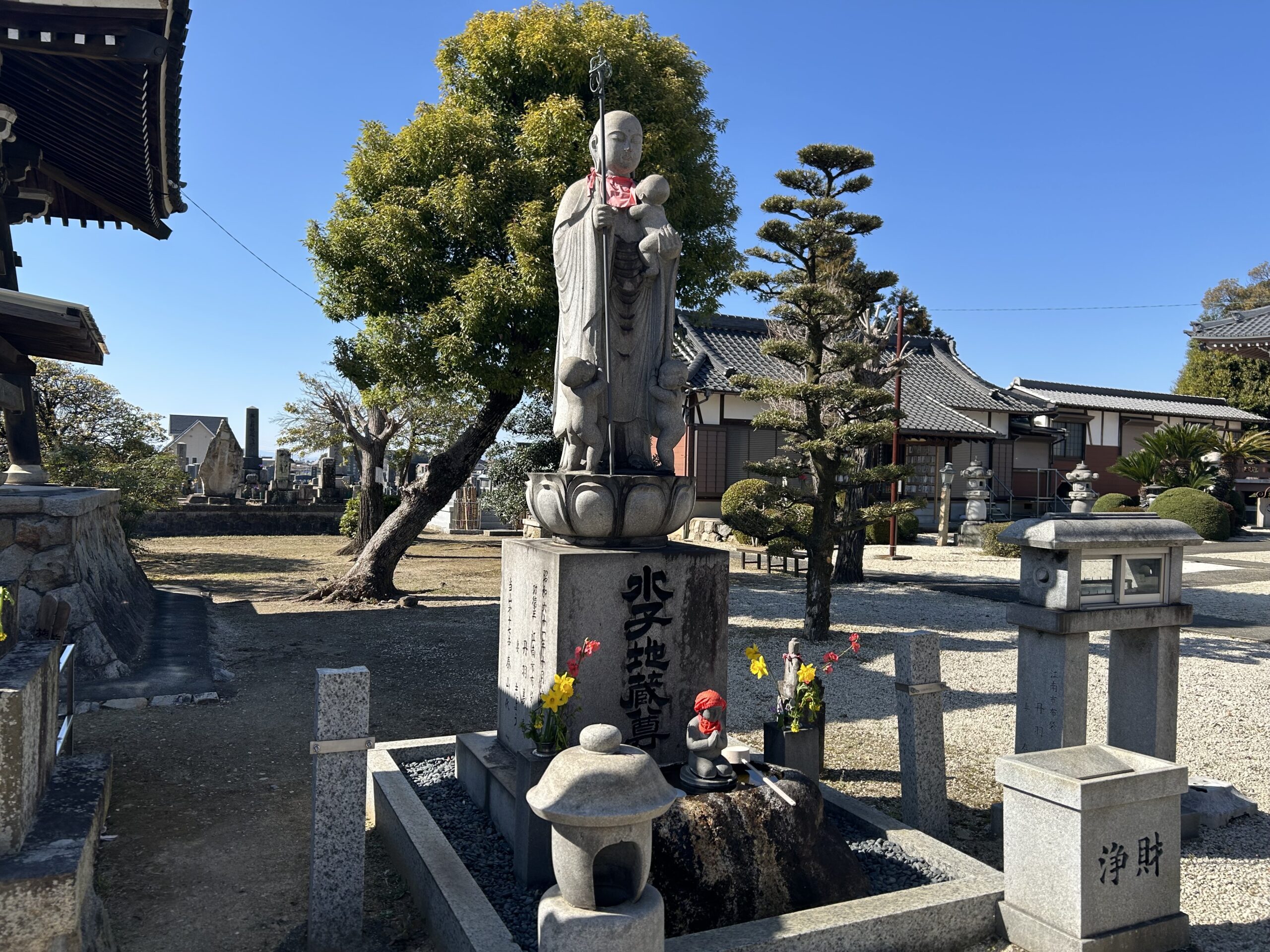桜越しに見る水子地蔵 赤い前掛けをまとう石仏